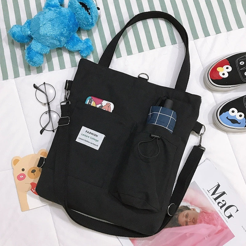 Black canvas tote bag with front pocket and drawstring, plaid patch detail