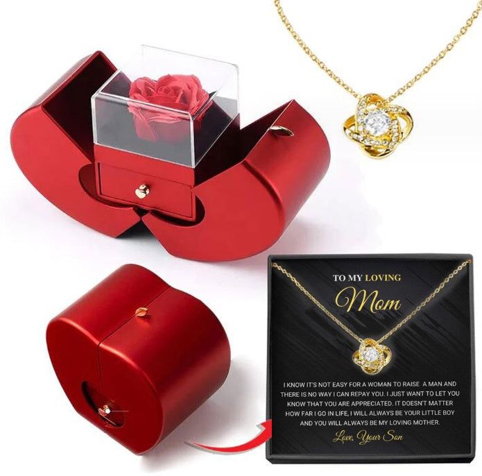 Red jewelry box with clear cover holding a red rose; gold heart pendant necklace shown