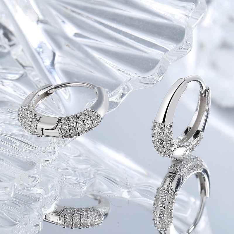 Sterling silver hoop earrings with dense zircon pavé on curved front, angled view